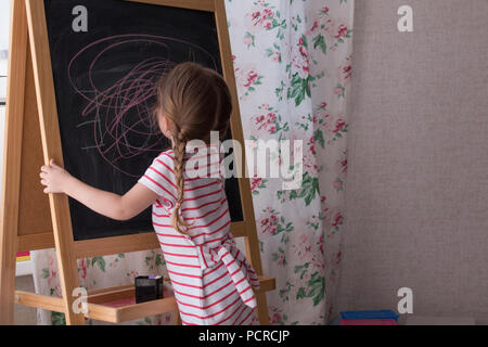 Little Preschool Girl Writing on Blackboard. Toddler girl holding chalk and drawing. Stock Photo