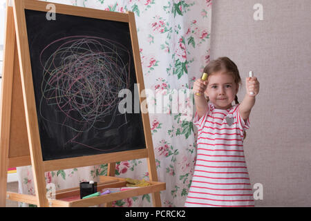 Little Preschool Girl Writing on Blackboard. Toddler girl holding chalk and drawing. Stock Photo