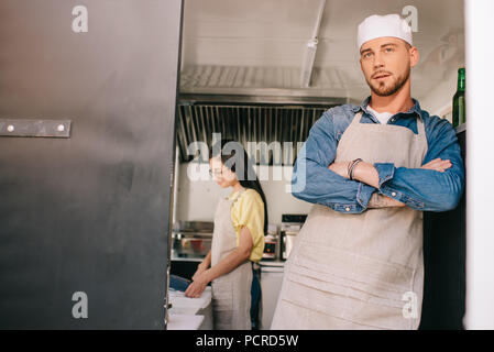 male chef standing with crossed arms while female colleague working behind in food truck Stock Photo