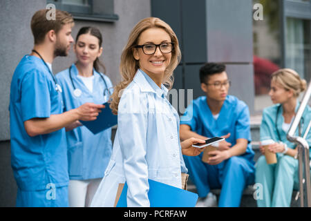 smiling teacher looking at camera, multicultural students talking near medical university Stock Photo