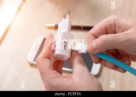 White charger with USB cable in hands with smartphone in background Stock Photo