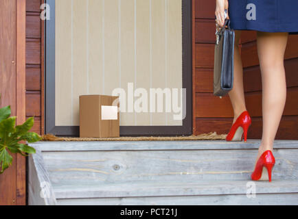 Woman arrives home after work with briefcase to find a delivery parcel with label at door Stock Photo