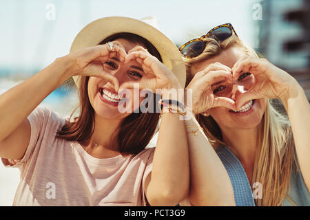 Two smiling young friends making heart shapes with their hands while having a fun day out together in summer Stock Photo