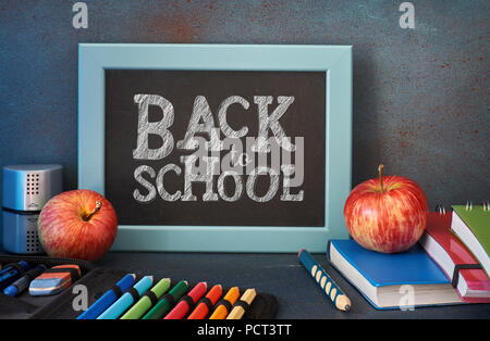 Stationery, apples and books  on wooden table in front of blackboard with text "Back to school" Stock Photo