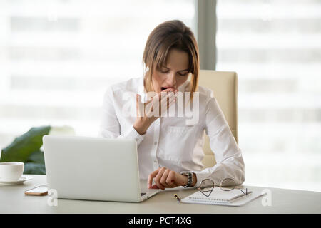 Exhausted female employee checking time on watch in office Stock Photo