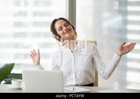 Happy female worker enjoying favorite music at work Stock Photo