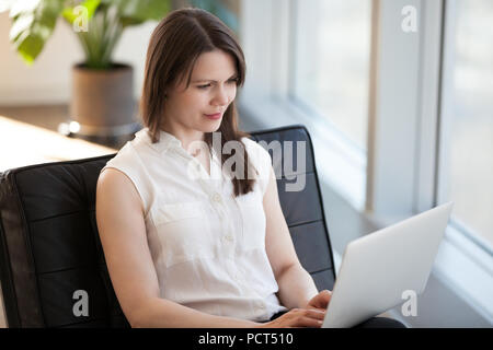 Successful woman busy working at laptop sitting in chair Stock Photo