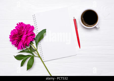 Empty notepad with place for text, pen, a cup of coffee and peony flower on a white wooden background. Mockup for your design. View from above. Stock Photo