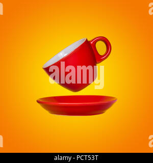 Creative surreal design with a red coffee cup and saucer on a yellow background. A cup and saucers flying in the air. Stock Photo