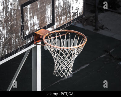 Close up view of a weathered old orange basketball hoop and net from above on playground in Europe with white painted backboard with black borders Stock Photo