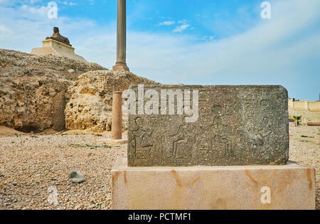 The stone panel with carved Egyptian hieroglyphs in Amoud Al Sawari (Serapeum) archaeological site with Pompey's Pillar and sphinx statue on backgroun Stock Photo