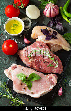 Fresh raw meat. Different types of raw pork meat, chicken fillet and beef with vegetables and herbs on dark wooden background. Stock Photo