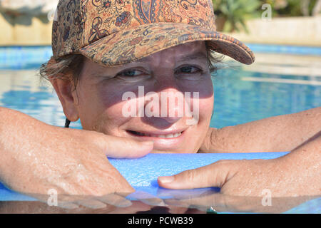 Woman, holding a pool noodle floating in a swimming pool, smiling to camera Stock Photo