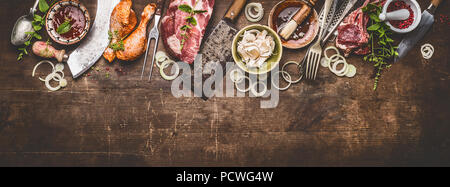 Various grill an bbq meats on rustic wooden background with aged kitchen and butcher tools, herbs, spices, seasoning and sauce, top view, border Stock Photo