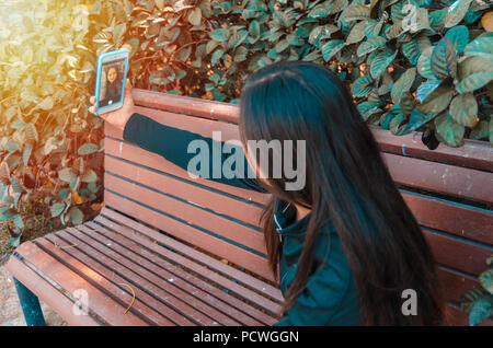 Young lady taking selfie on a bench using her smart phone Stock Photo