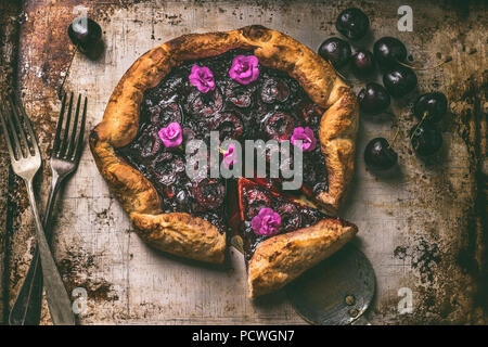 Top view of homemade open cherry pie or galette on aged baking tray background with cutlery, top view. Summer berries still life concept Stock Photo