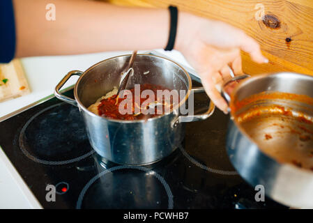 View of Woman Preparing a Tomato Sauce For Pasta in The Kitchen Stock Photo