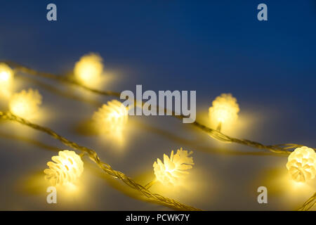 Blurred yellow christmas lights in shape of cones in three rows on dark background , low depth of focus. Stock Photo