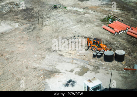Orange excavator standing on a ground during construction of a new building in the city area. Aerial view on a construction building place. Construction machinery Stock Photo
