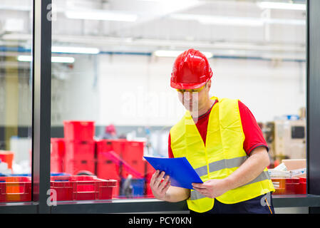 Factory supervisor in yellow reflective west with red helmet. Factory supervisor looking at blue folder with documents Stock Photo