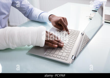 Close-up Of A Businessman With Bandage Hand Using Laptop At Workplace Stock Photo