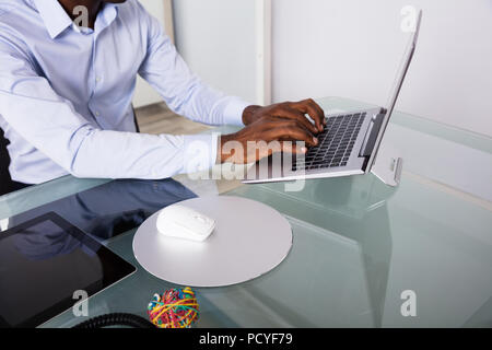 Close-up Of Businessman's Hand Typing On Laptop Over The Reflective Desk Stock Photo
