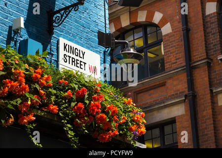 Sign for Kingly Road on a blue painted brick wall, building decorated with flowers, Carnaby, London, UK Stock Photo