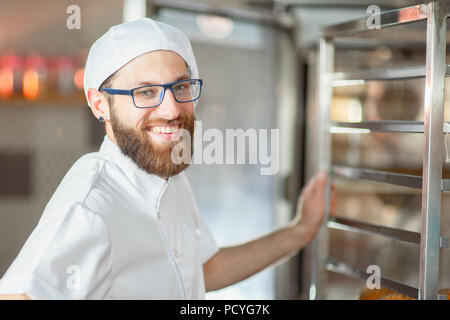 Portrait of a young beautiful baker with fresh bread and an oven in the background. Stock Photo