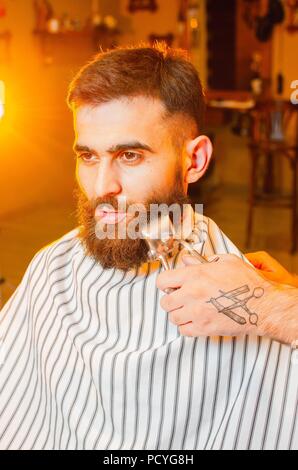 Barber cuts a beard of vintage hair clippers to a young handsome guy with a beard and mustache. Men's hair salon. Stock Photo