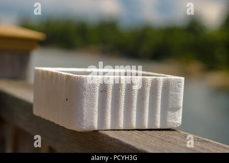 A styrofoam bait worm container on a ledge next to a lake ready to