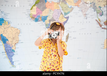 little caucasian boy taking picture with vintage film camera on world map background