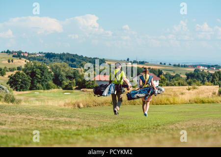 Full length rear view of a couple carrying golf bags Stock Photo