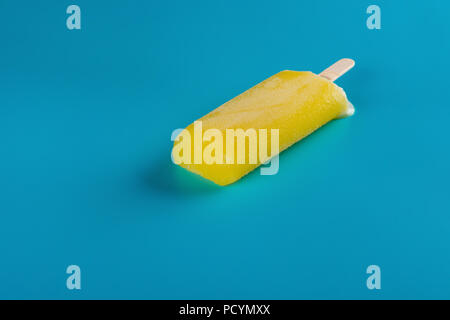 side view yellow popsicle starts melting on blue background Stock Photo