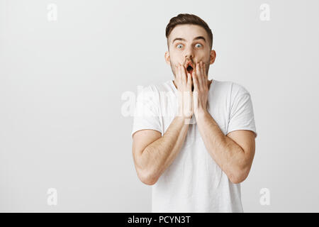 Omg so exciting. Portrait of impressed speechless over-emotive handsome male with cool haistyle in white t-shirt folding lips in wow sound holding pal Stock Photo