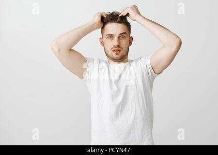Hair is huge mess. Portrait of shocked and worried guy staring at camera touching strands of haircut and opening mouth being dissatisfied with new hai Stock Photo