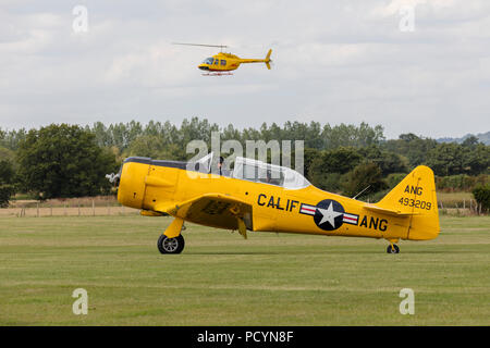 Side view of a historic North American T-6 Texan Harvard aeroplane with a DHL helicopter hovering in the background Stock Photo