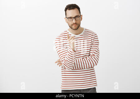 Indoor shot of determined creative businessman in black glasses and striped shirt, pointing at camera with index finger and looking seriously, giving  Stock Photo