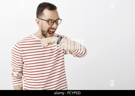 Funny yelling european man in glasses, raising arm near face and shouting at black digital watch, making command to personal assistant or talking with Stock Photo