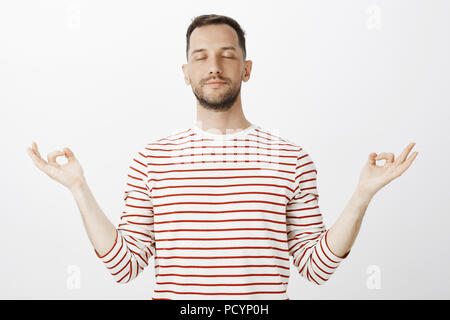 Trying to find peace inside body. Portrait of calm relaxed handsome husband, closing eyes and spreading hands aside with zen gesture, meditating or pr Stock Photo