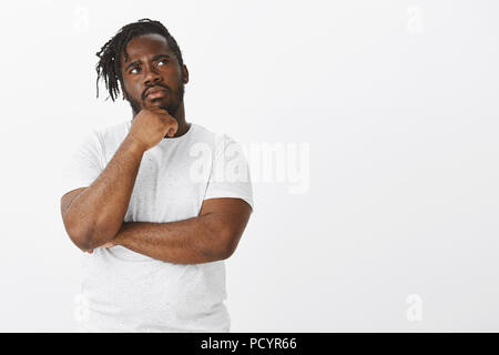 Choices and opportunities everywhere. Portrait of focused thoughtful young and plump african-american, touching chin with hand and staring frowned at  Stock Photo