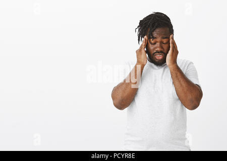 Guy trying to focus and concentrate on task. Unfocused tired plump dark-skinned guy with beard and moustache, closing eyes and touching temples, havin Stock Photo