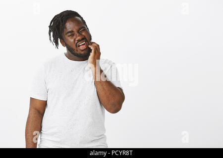 Boyfriend unsure how to refuse offer. Portrait of doubtful attractive plump guy, scratching beard and tilting head while looking down, being shy or em Stock Photo