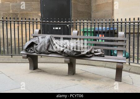 A bronze sculpture of a “homeless Jesus” sleeping rough on a bench in Nelson Mandela Place, Glasgow city centre, Scotland, UK. Stock Photo