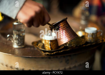 Serving Turkish coffee which cooked in hot sand from a copper cezve to golden Turkish coffee cups. Stock Photo