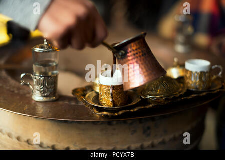 Serving Turkish coffee which cooked in hot sand from a copper cezve to golden Turkish coffee cups. Stock Photo