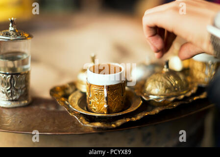 Serving Turkish coffee which cooked in hot sand from a copper cezve to golden Turkish coffee cups. Stock Photo