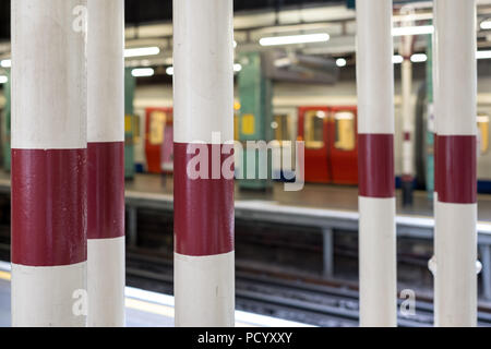 Platform at Aldgate Underground Station, London showing painted pillars and train in soft focus waiting on platform in the background. Stock Photo