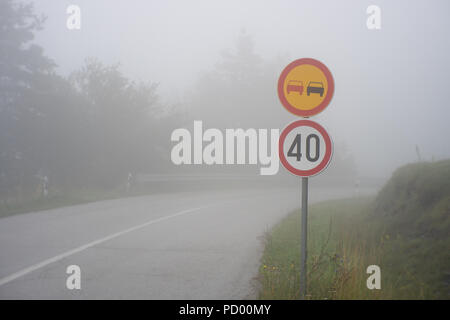 Traffic sign showing speed limit on misty road with poor visibility. Road through the foggy forest Stock Photo