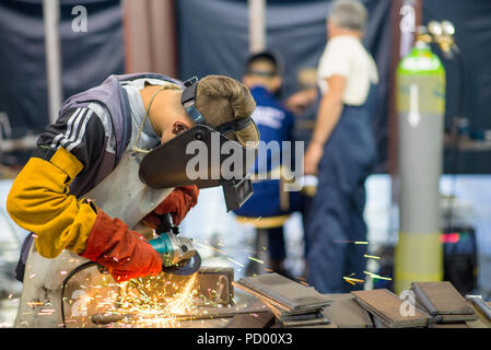 Belgrade, Serbia - May 23, 2018: Welder working in a factory with two blurry workers in the background Stock Photo