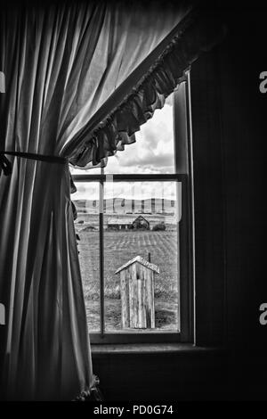 A unique view of a rural outhouse, through the old farmhouse window of the main house to which it belonged. Original photo has been desaturated to inc Stock Photo